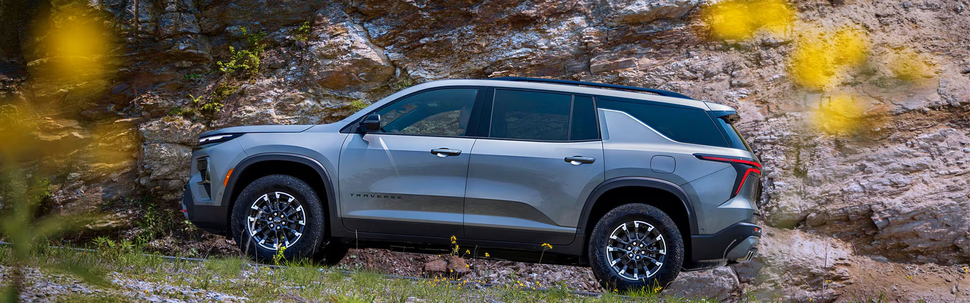 2026 Chevrolet Traverse in gray parked on a scenic roadside with rocky cliffs and greenery visible behind it.